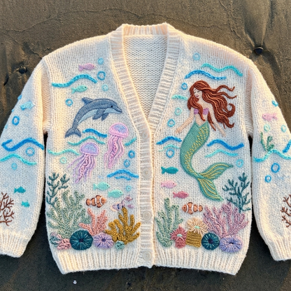 Knitted cardigan with mermaid and ocean creature design on a dark surface