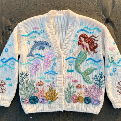 Knitted cardigan with mermaid and ocean creature design on a dark surface