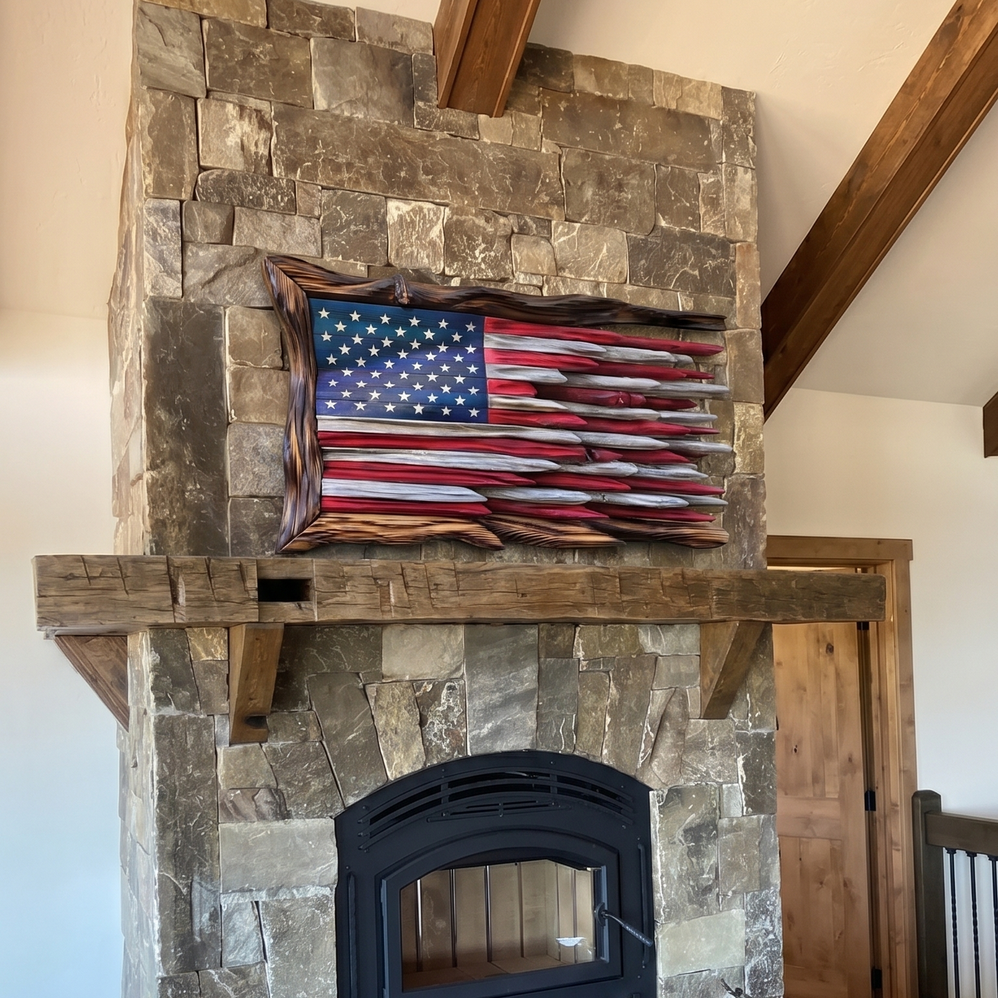 Stone fireplace with American flag artwork above it in a room with wooden beams.